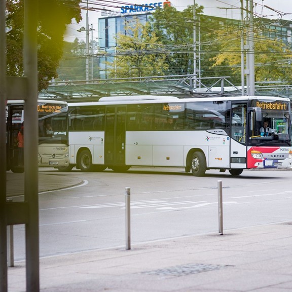Salzburg Transport Association bus at a bus stop near Salzburg Central Station with overhead lines and buildings in the background.