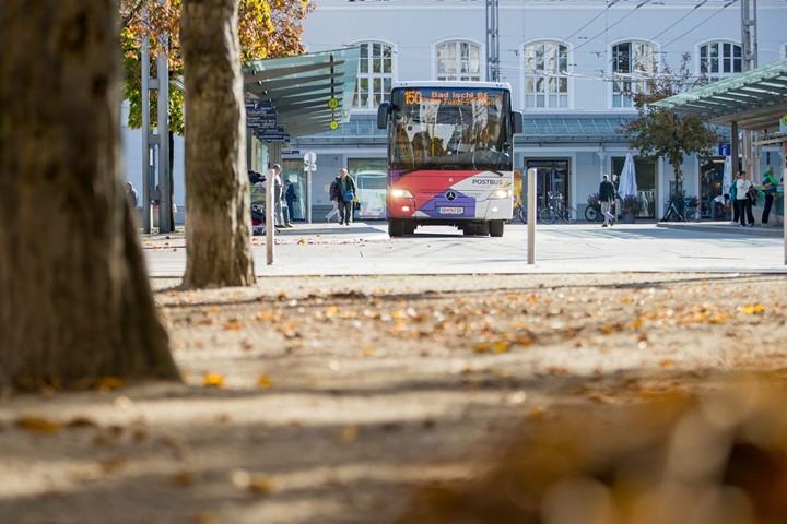 Bus at bus stop in front of Salzburg Central Station, passengers waiting under covered platform.